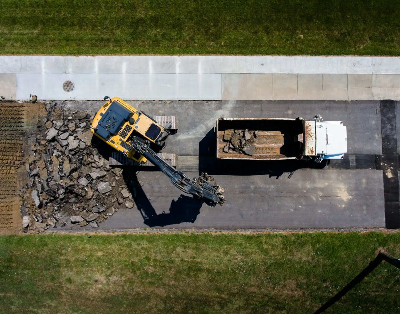 Luftbild: Bagger arbeitet neben einem LKW auf einer Fahrbahn