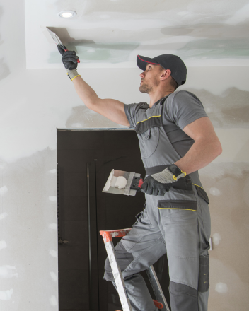 Ein Handwerker spachtelt Deckenfugen mit Kelle und Spachtel in einem Raum im Ausbau