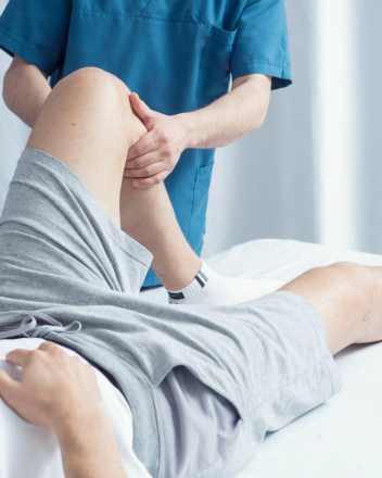 Physiotherapeut in blauer Kleidung mobilisiert das gebeugte Bein eines liegenden Patienten