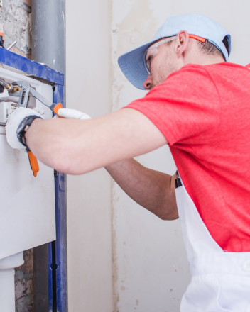 Handwerker in rotem Shirt und blauer Kappe arbeitet mit einem Werkzeug an einer Wandinstallation