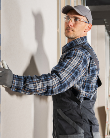 Handwerker mit Schutzbrille und Kappe streicht eine Wand, sein Schatten fällt darauf