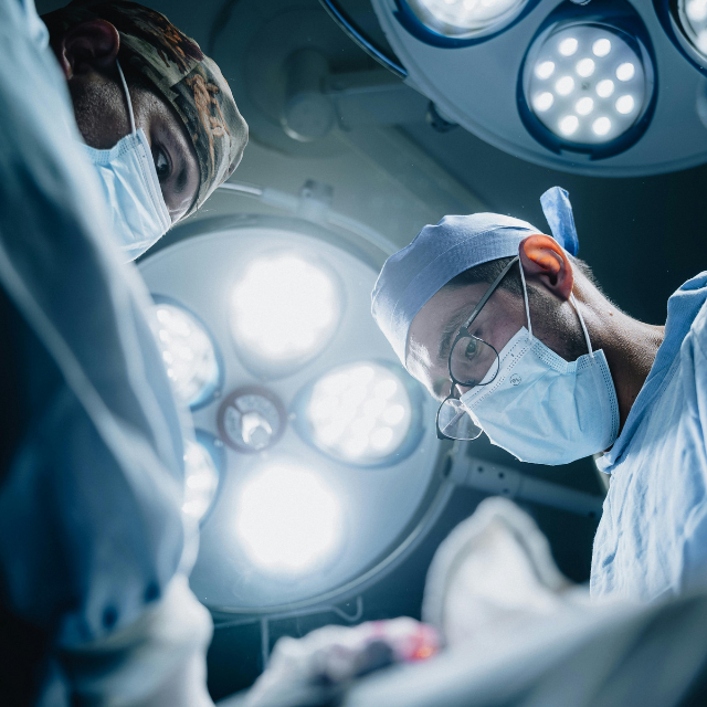 Zwei Chirurgen mit Mundschutz und OP-Licht über dem Patienten im Operationssaal