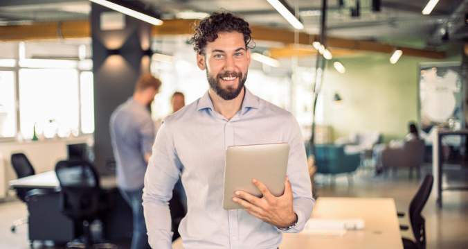 Lächelnder Mann im Büro hält ein Tablet vor sich
