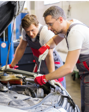 Zwei Mechaniker prüfen den Motorraum eines Autos, einer schraubt mit Ratsche