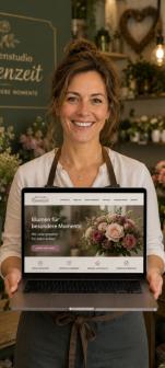 Lächelnde Floristin hält einen Laptop mit Blumenladen-Website vor Blumenregal im Hintergrund