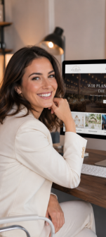 Lächelnde Frau im hellen Blazer am Schreibtisch vor einem Computerbildschirm